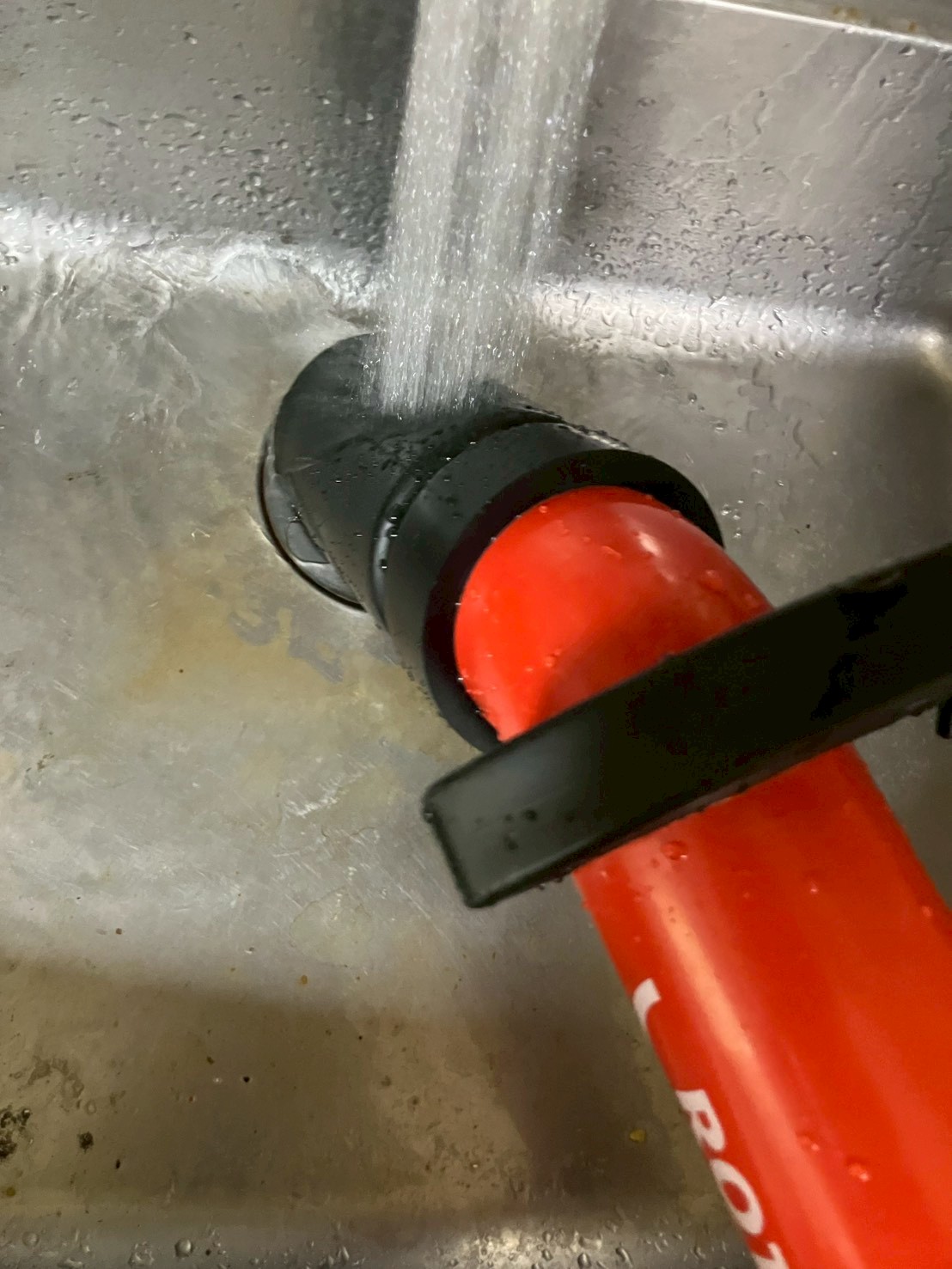 赤いローポンプをキッチン排水口に当てて加圧・減圧による詰まり除去作業中