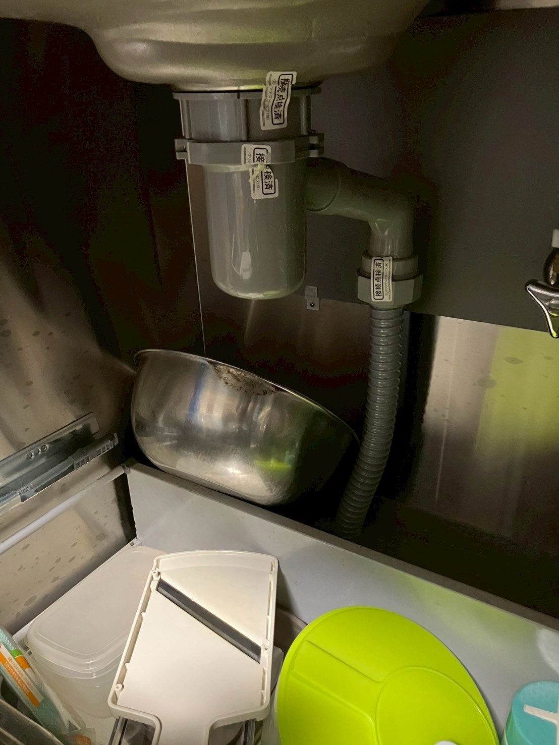 シンク下収納内部。ABS製排水トラップと蛇腹ホース。水受け用のステンレスボウルが置かれている