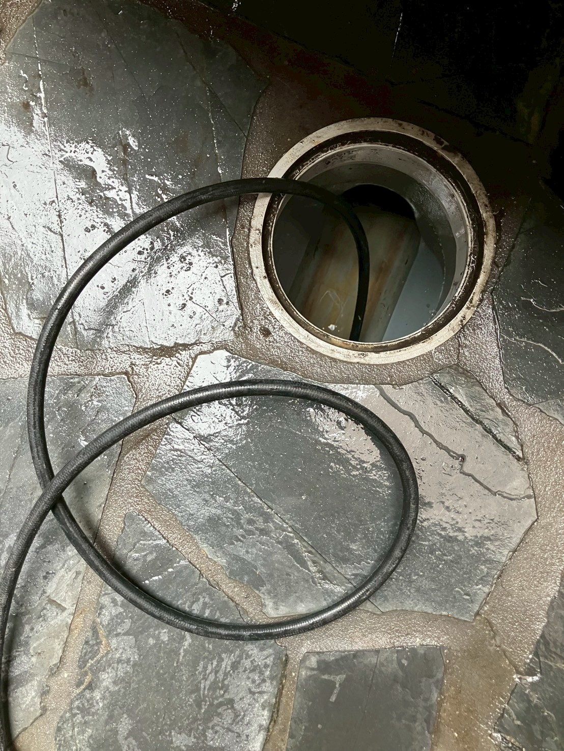 屋外石畳タイル面の排水桝開口部に高圧洗浄ホースを挿入して洗浄中。周囲が作業水で濡れている