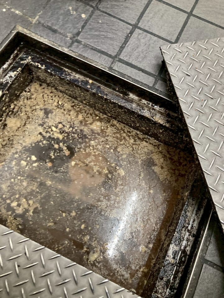 グリストラップ内部。油脂と汚泥が分厚く堆積し、底面がほぼ見えない状態