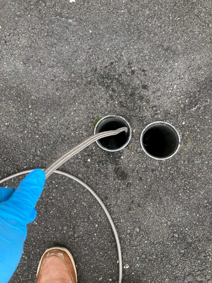 屋外アスファルト面の排水管開口部2か所にスネークワイヤーを挿入している作業中の写真
