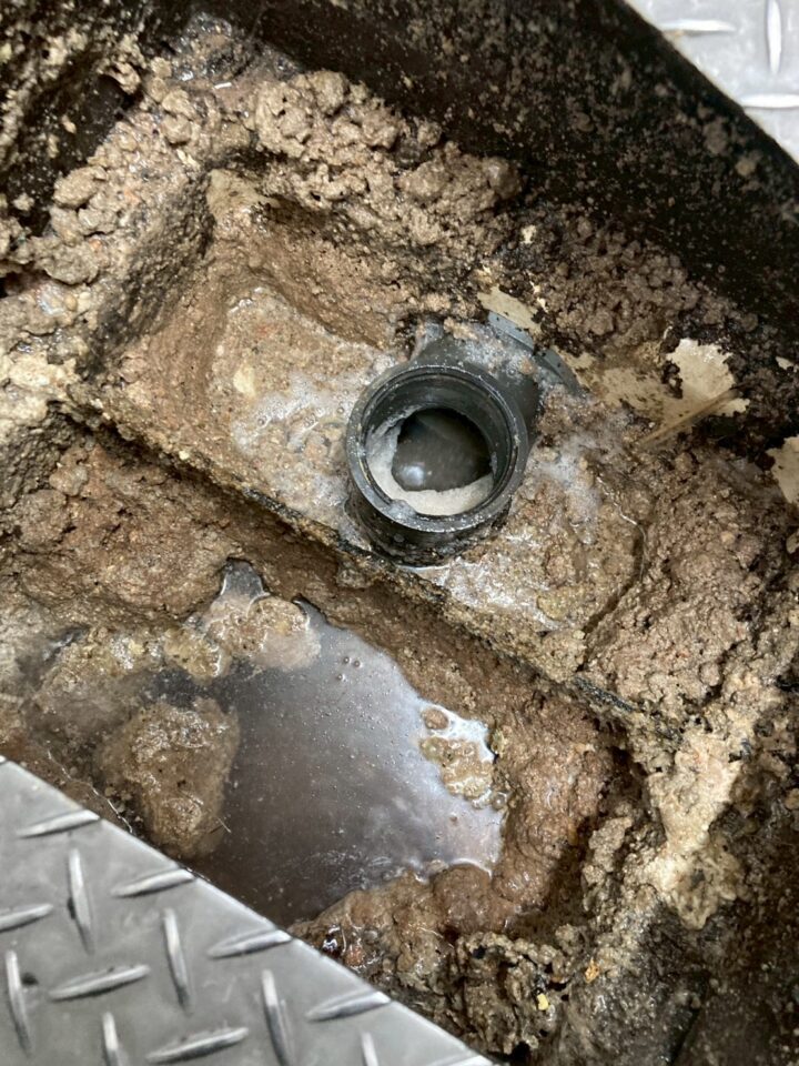 グリストラップ底部の排水管接続口の拡大。油脂・汚泥の固形物が管口周辺をほぼ完全に塞いでいる