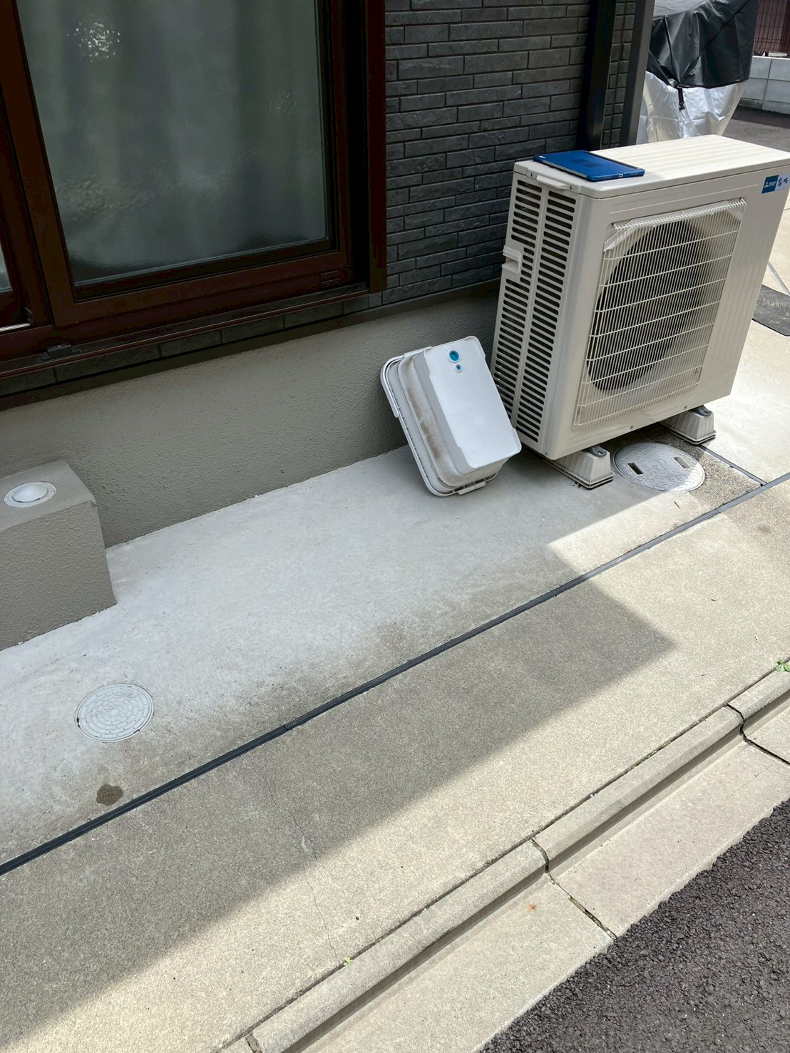 京都市南区N様宅の外構。コンクリート敷きの外構に排水桝の蓋が見える。白い樹脂製の蓋が取り外されて壁際に立てかけられている