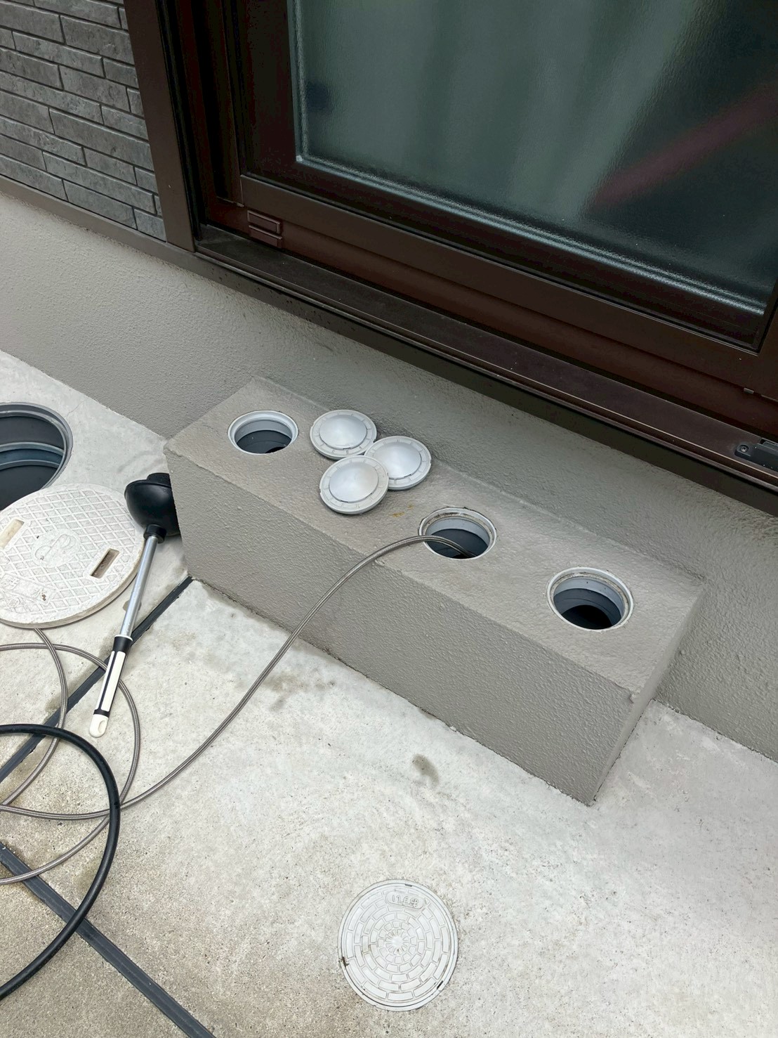 建物基礎外壁部分に4本の塩ビ配管が露出。キャップが外されスネークワイヤーが挿入されている。各配管系統の詰まりを確認している