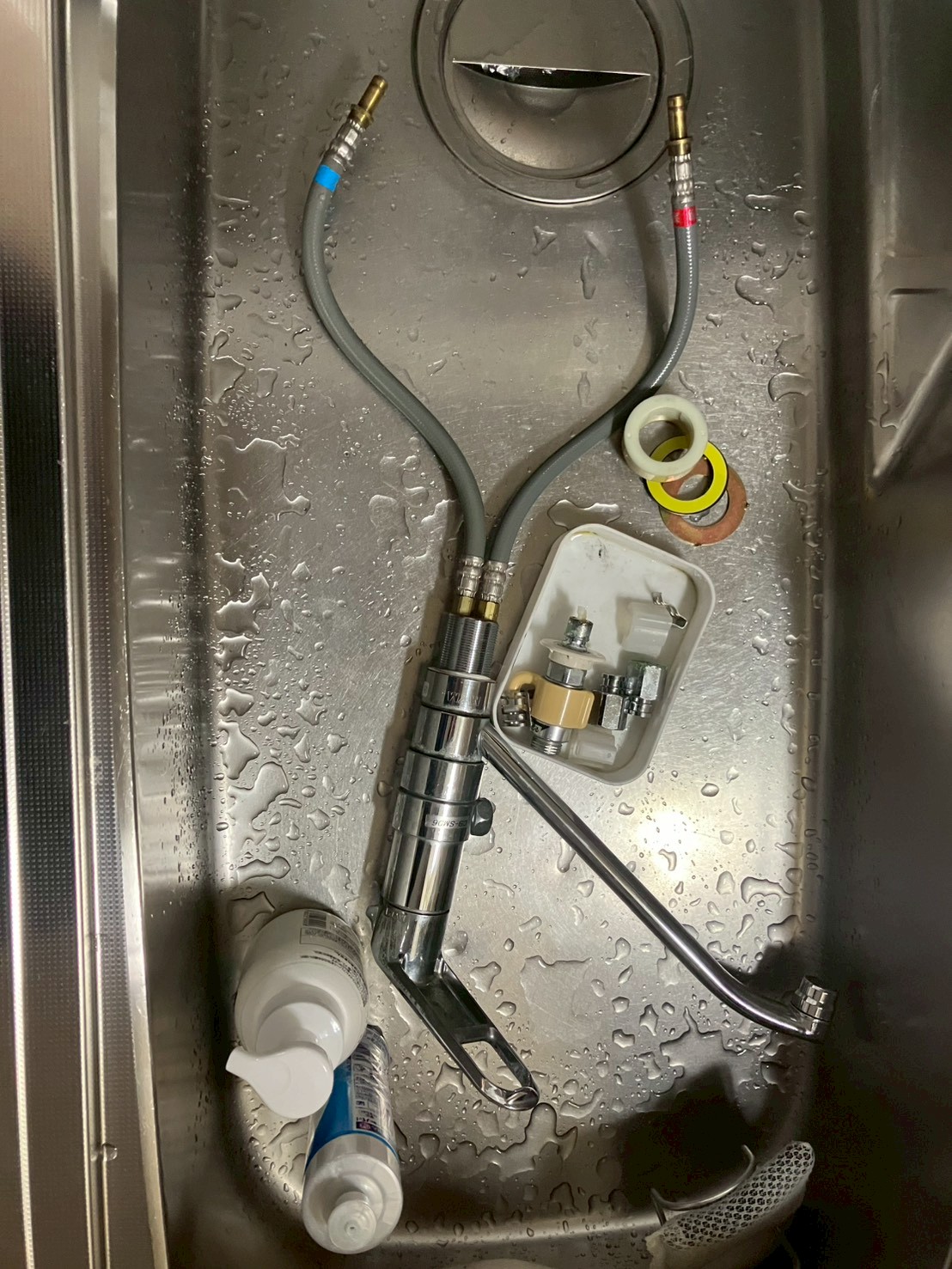 取り外した旧水栓本体・給水ホース・分岐アダプター・パッキン類がシンクに置かれた状態