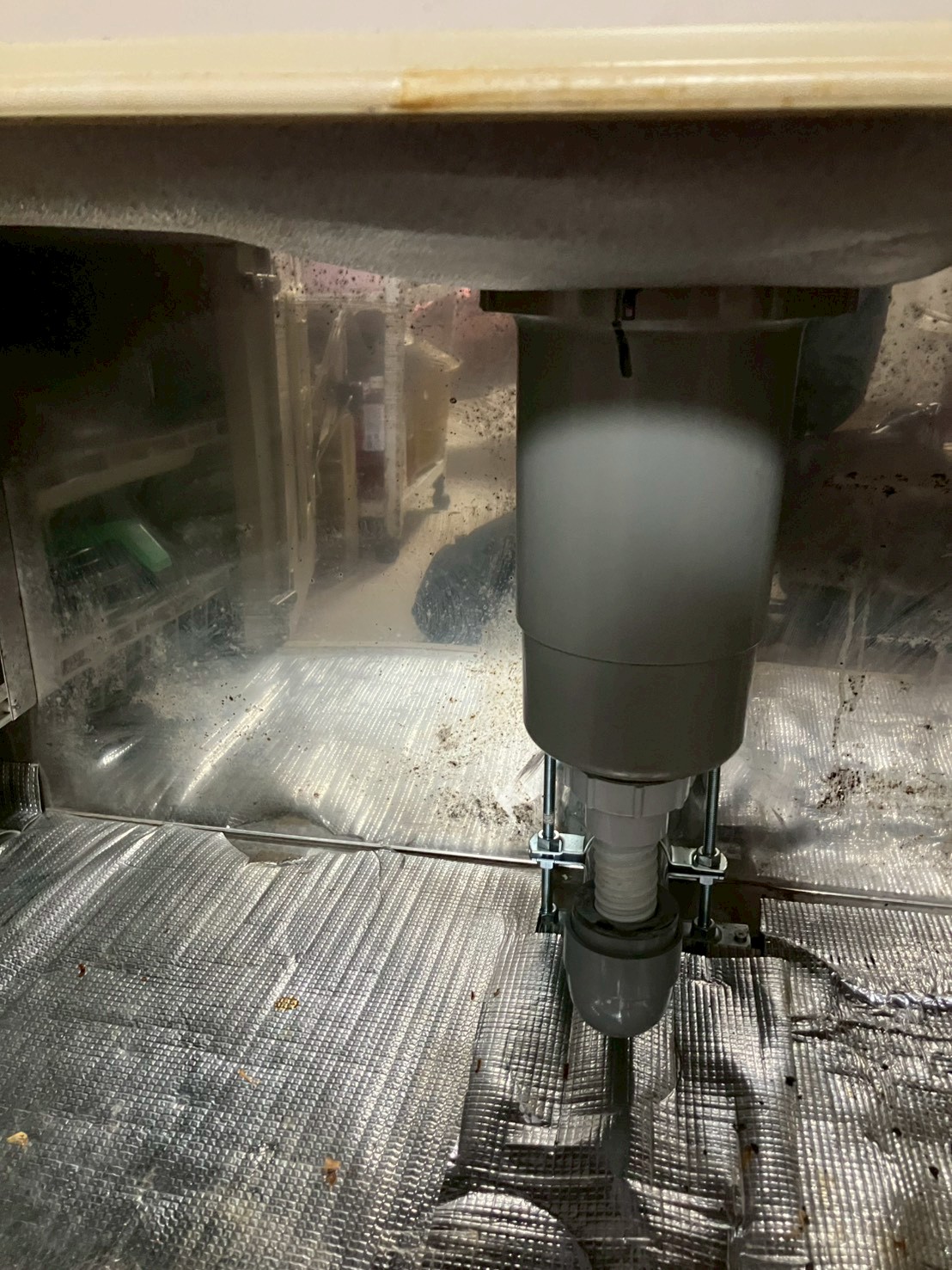 シンク下キャビネット内部。新しい水栓の取付ナット部分が確認でき、内部は結露・汚れで覆われている