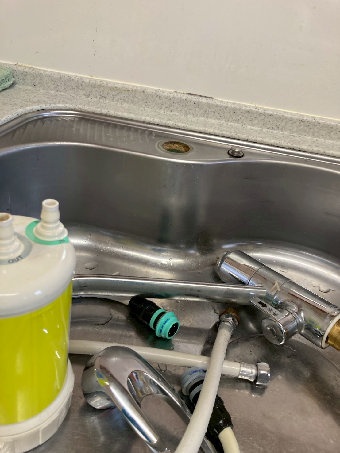 キッチン水栓取り外し作業中。旧水栓本体と浄水器・接続ホース類がシンクに取り出されている
