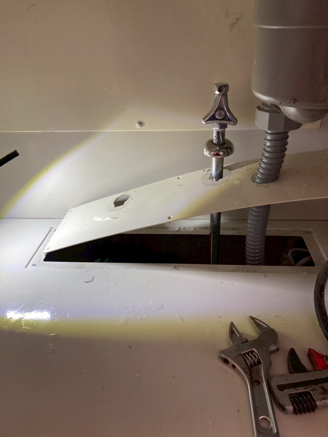 シンク下の床下点検口を開けて止水栓取り外し作業中。スパナ・モンキーレンチを使用