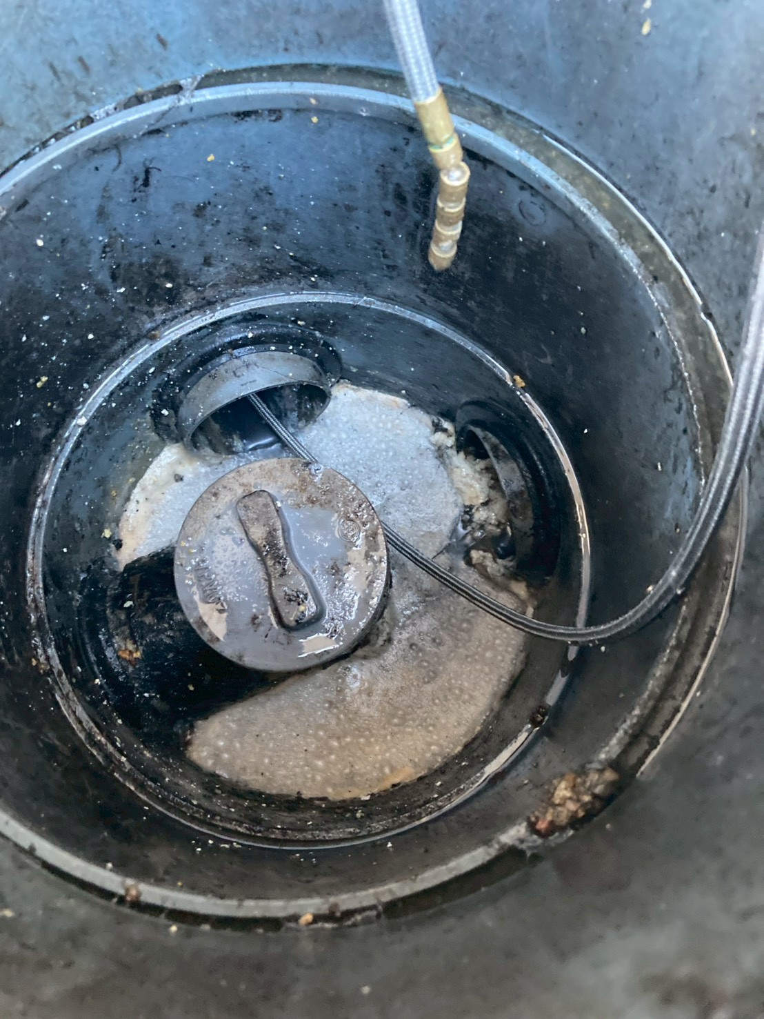 屋外の排水桝の内部に高圧洗浄ホースを挿入し、油脂や汚泥を洗い流している様子