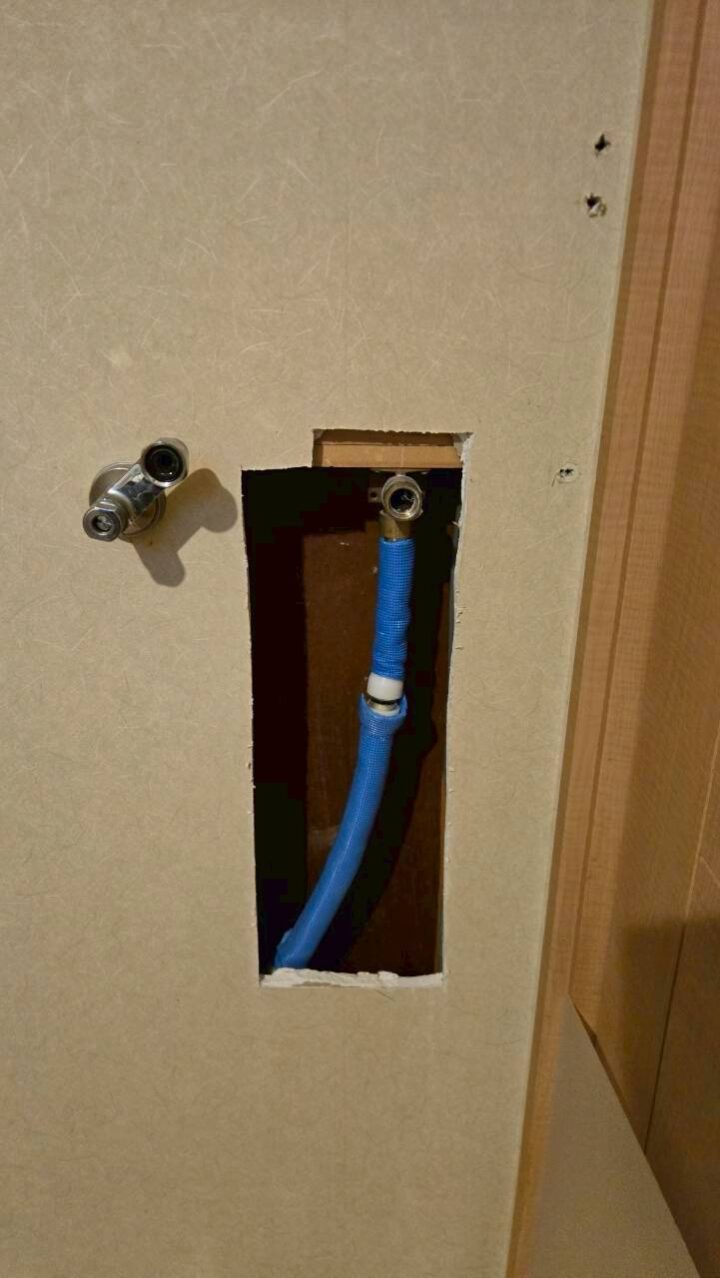 壁の開口部から青いポリ管と止水栓の接続部を別アングルから撮影した施工中の様子