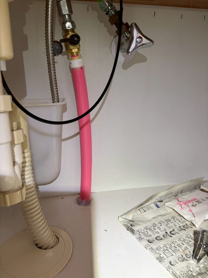 キッチンシンク下にピンク色の給湯フレキ管を引き込み、止水栓に接続している様子