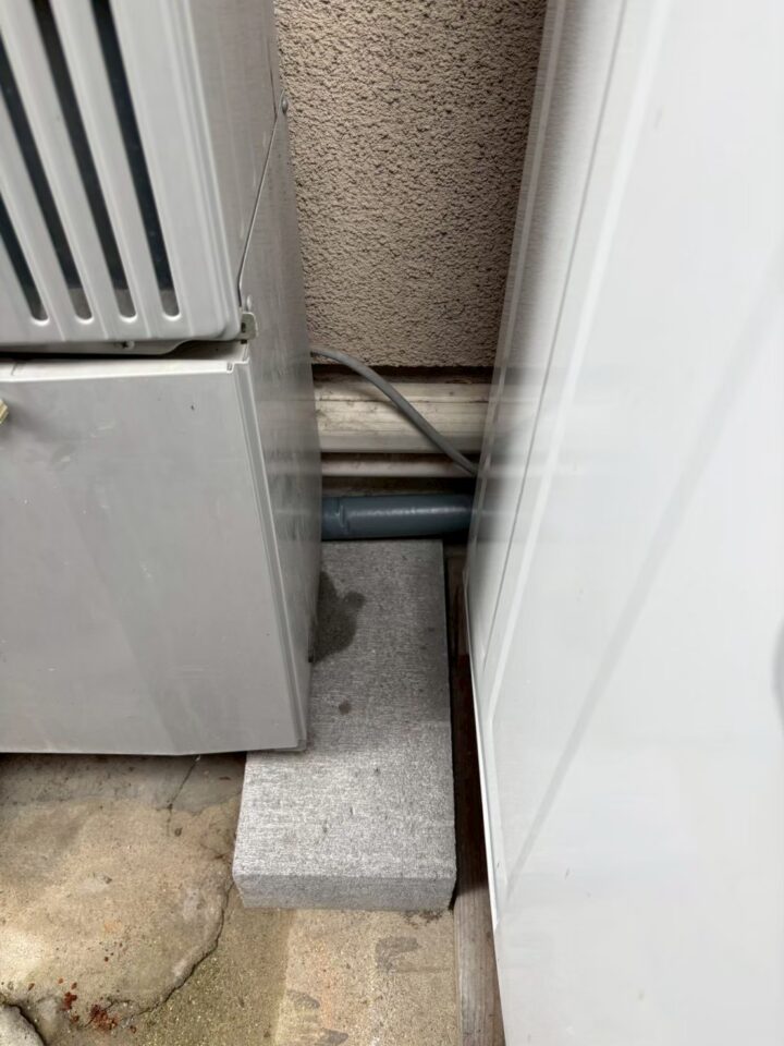外壁と扉の隙間に新設された配管が外壁を貫通している様子