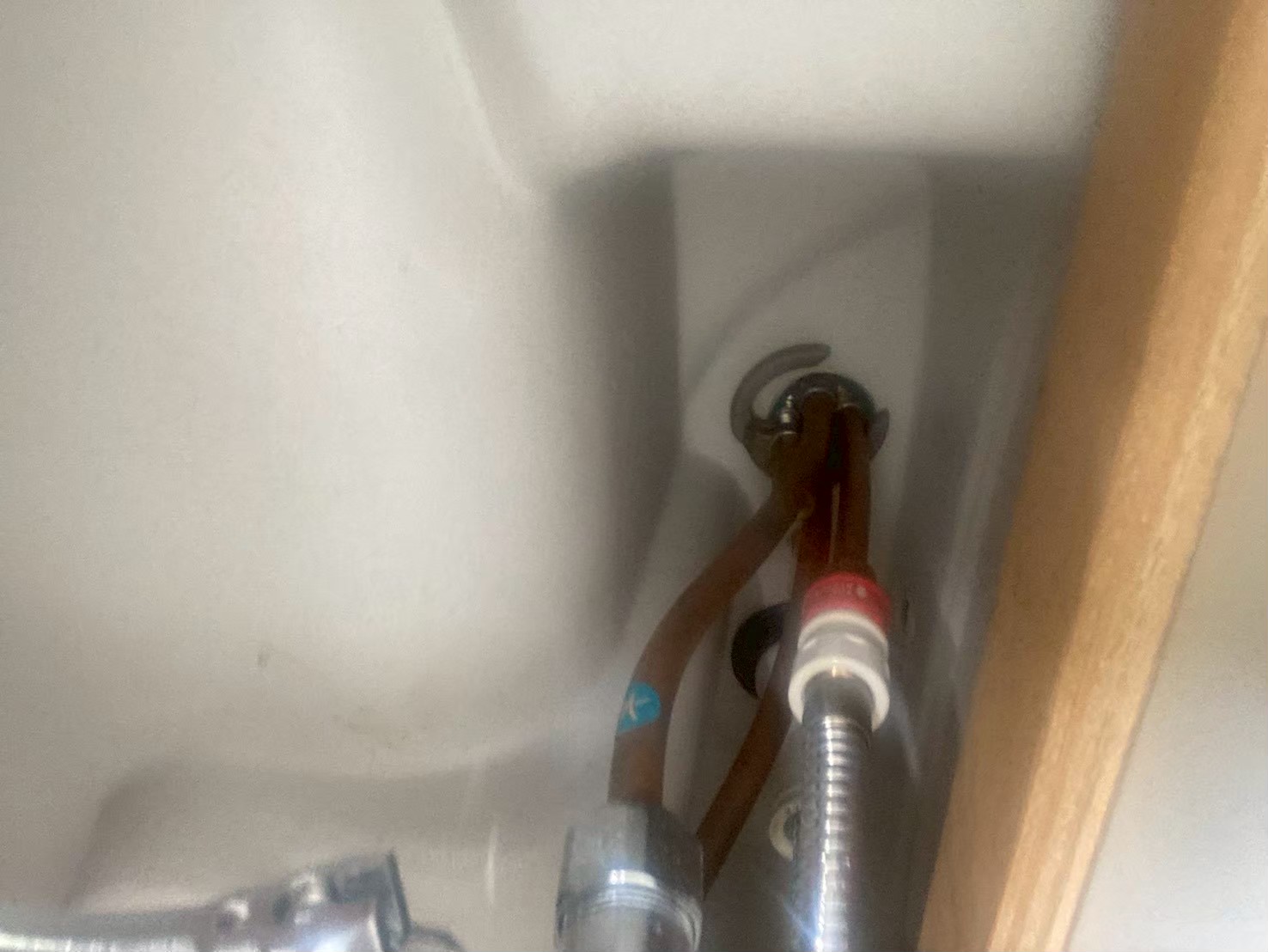 洗面台キャビネット内部の給水管接続部。銅管が赤茶色に腐食し、水漏れ跡の汚れが広がっている