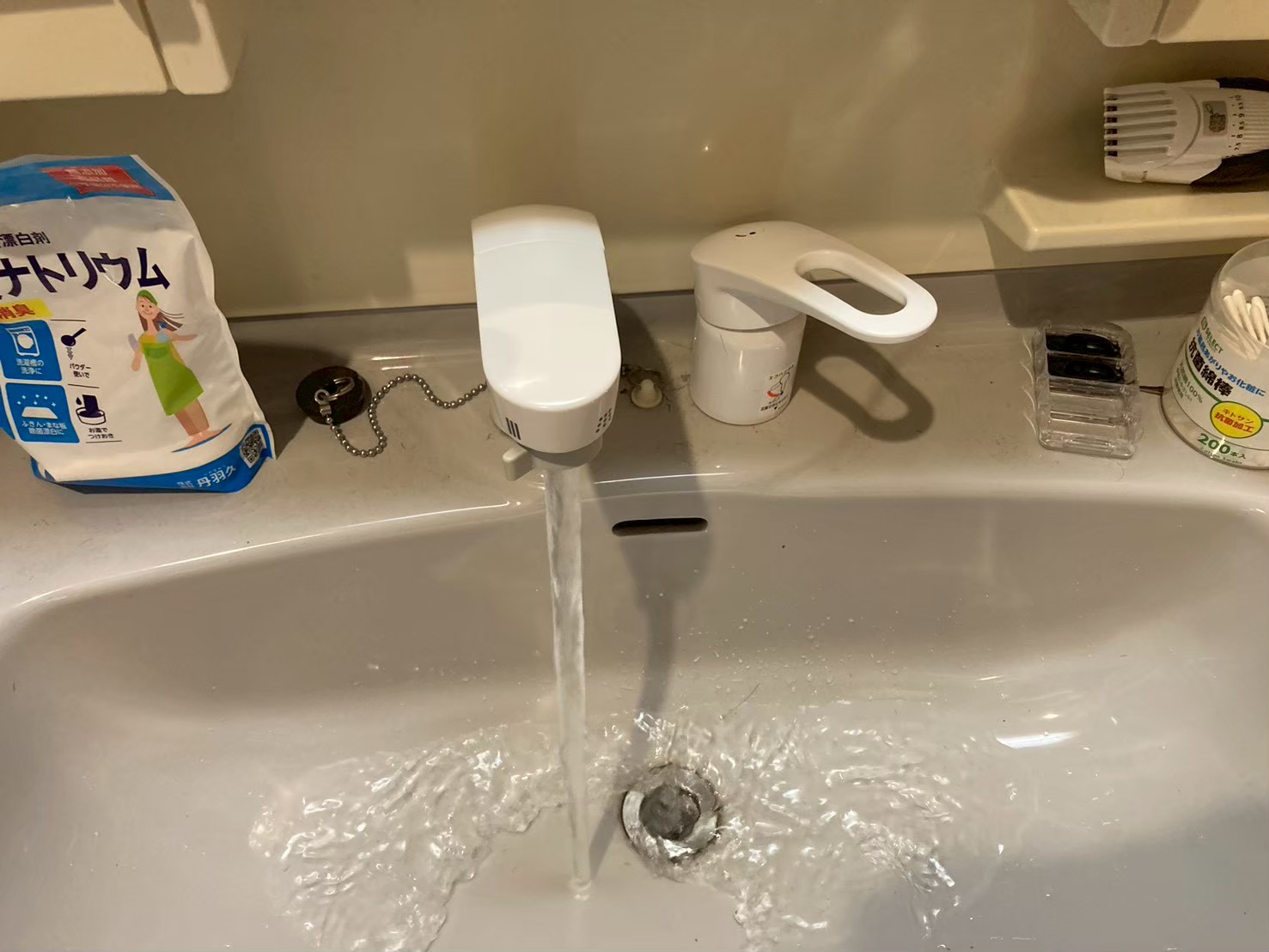 施工完了後の通水テスト。新しい白いシングルレバー混合水栓から水が流れ、洗面ボウルに水が流れ込んでいる