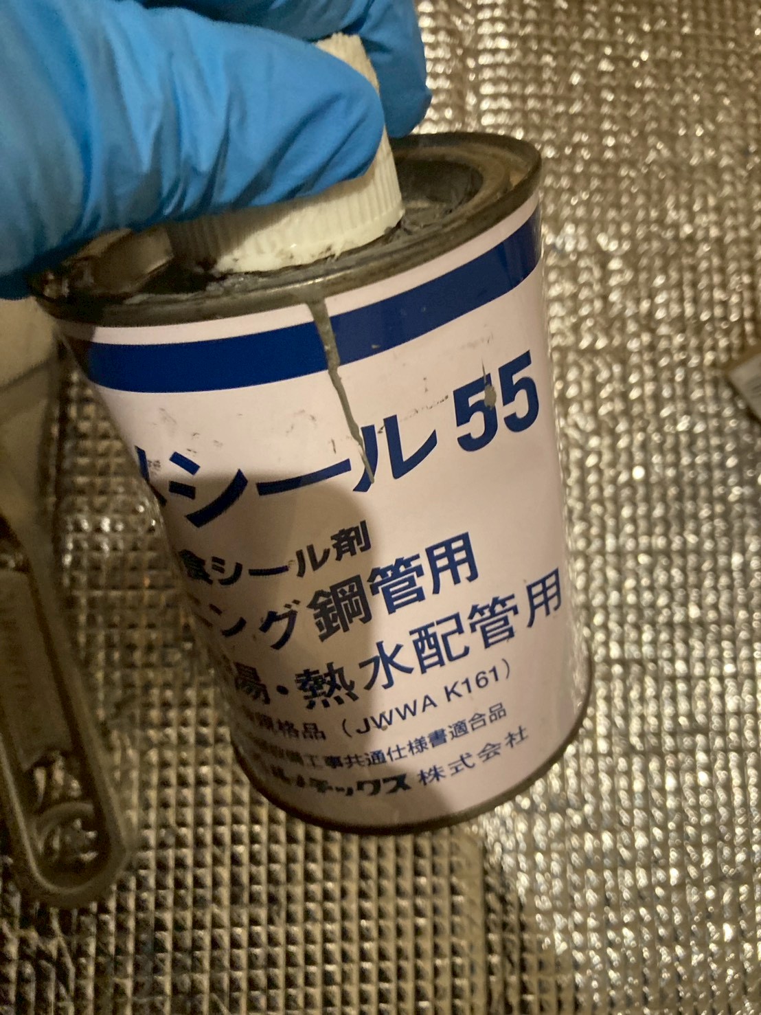 配管用ねじシール剤ロックタイト55（JWWA K161規格品）の缶を手で持っている場面