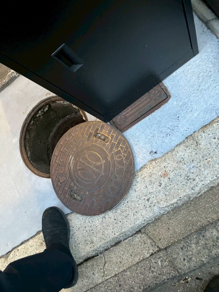 屋外の排水枡の蓋を開けた様子。錆びた鋳鉄製の丸形マンホール