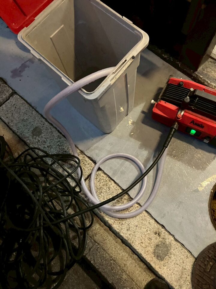 赤色のAsada製高圧洗浄機と洗浄ホース、回収用バケツが置かれた様子