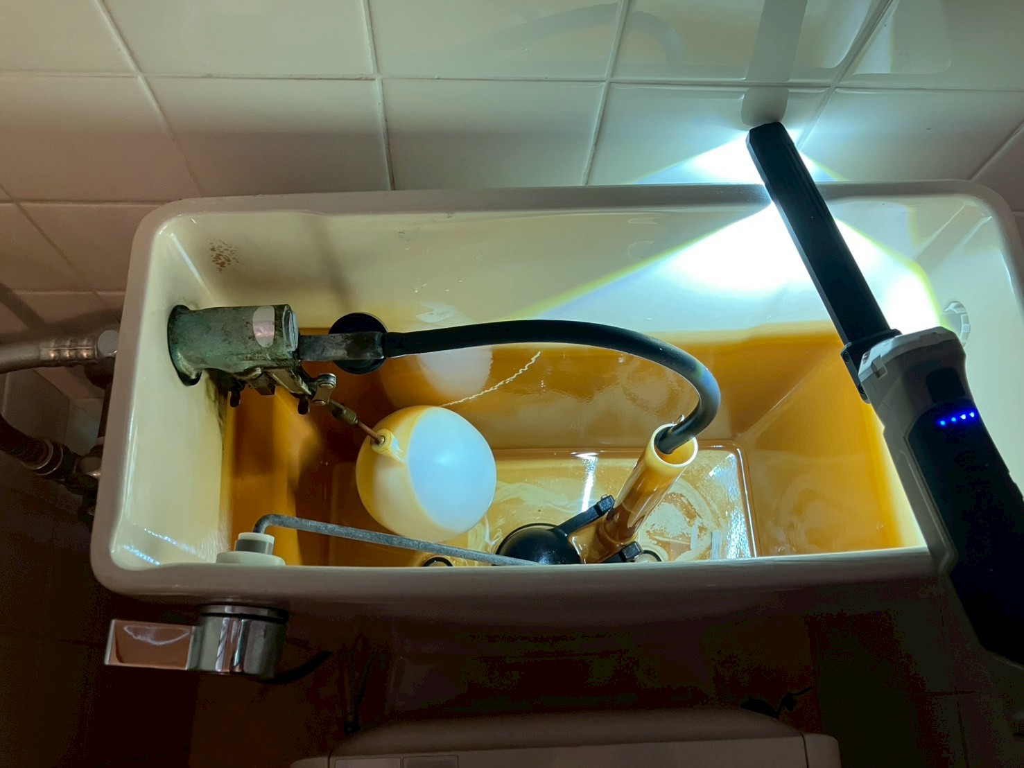 施工前のタンク内部。茶褐色に汚染された水の中に旧式の金属アーム型ボールタップ・フロートボール・フロートバルブが見える