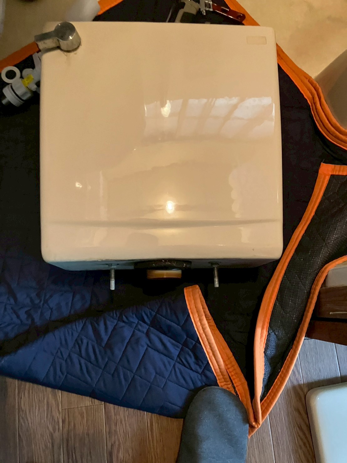 タンクを便器から取り外して養生シートの上に置いた状態。タンク底部の排水口フランジとボルト2本が確認できる