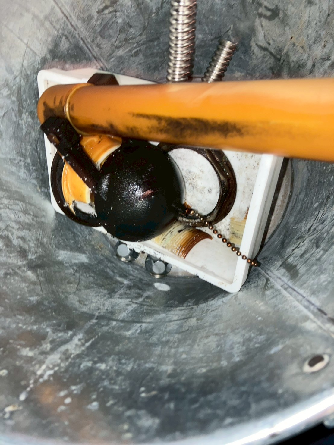 タンク底部の排水口部分のアップ。旧フロートバルブ座のゴムとオレンジ色のサイフォン管が劣化した状態で確認できる