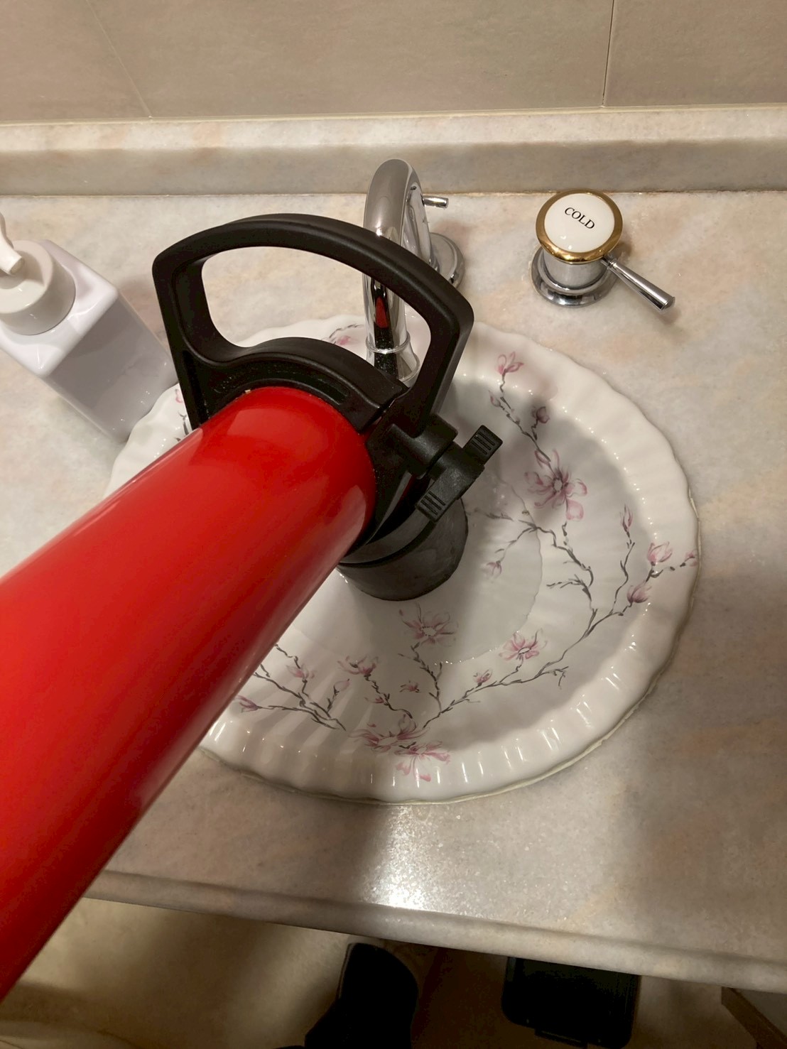 赤色のトーラー機（電動ワイヤー式詰まり除去機）を手洗い器の排水口に当てて作業している様子