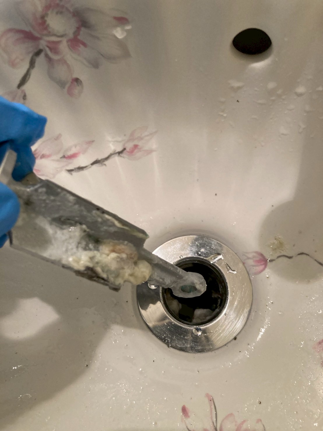 排水口からヘラで白い石鹸カス・スケールの塊を掻き出している作業中の様子。ゴム手袋を着用