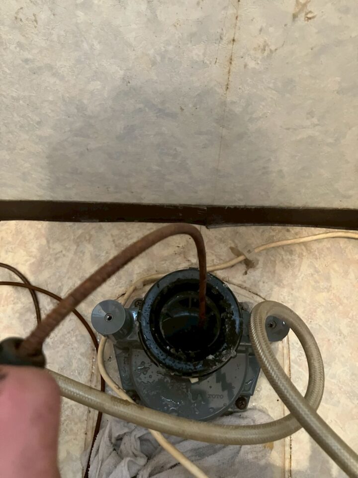 床フランジの排水口に高圧洗浄ホースを挿入して詰まり除去作業中