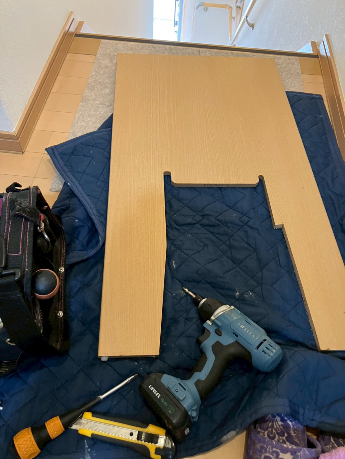 廊下にブルーシートを敷いて養生し、取り外した便器パネルと工具類が置かれている